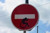 A No Entry sign with the white bar being carried by a wheelchair user