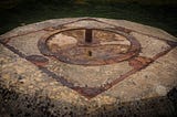 Moody photograph of a strange object resembling a ritual site, comprised of rusting metal embedded in concrete.