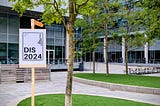 Photo of the conference entrance, showing a DIS 2024 sign, some trees, and the building and entrance.
