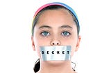 Girl with duct tape on her mouth. The tape has the word secret on it.