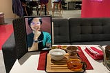 iPad stands vertically with a person, Chris, on it, with full bust and face visible. There is a small tea table with tea on it neaaryby.