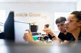 Two people looking at a computer monitor in an office.