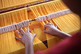 a loom with yellow threads and a woman’s hands