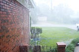 Rain pouring down side of brick house.