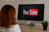 A woman sitting in front of computer screen with YouTube logo