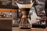 A barista pour hot water into a Chemex coffee brewer to make fresh, great-tasting coffee.