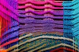 Adobe Firefly generated image with the prompt: Generate an image of a loom weaving threads into a patterned tapestry, where the threads are lines of code, showing how Generative AI weaves together different threads of data to form a coherent output. Use a palette of vibrant colors to represent the variety of data.