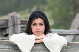 Woman leaning on the top of a fence looking at the camera