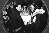 Two brothers at a wedding reception table, looking back to the camera.