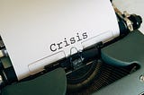 Antique typewriter sitting on a desk with one word written in bold on it: Crisis