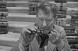 Screenshot of 1959’s Twilight Zone episode "Time Enough at Last", showing Henry Bemis holding his broken glasses amid books.