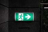A green and white exit sign displaying a stick-figure running towards an exit.