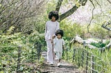 A Black woman, and her daughter, hold hands as they walk on a path at a park.