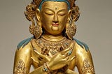 A golden figure of a Buddha, with a large golden crown, hands crossed on its chest.