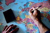 A person writing on a colorful world map.