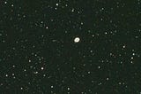 A bright oval shape in the middle of a dark star field. The oval is oriented with the long axis close to horizontal, slightly upward left to right. This is the Ring Nebula.
