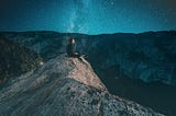 Person sitting on a rock looking out over a mountain range