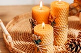 3 lit beeswax candles on a tray with a pine cone