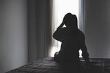 a woman wiht her back to a window. We can see her shadow and her hand is on her head. She looks sad. grief, family