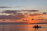 The silhouette of two people canoeing in the ocean against the backdrop of a beautiful, orange sunset in Utila.