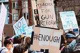 Protest signs that read “#Enough” “Teachers for Gun Reform” and “Guns Don’t Kill People, Umm…Yes They Do!”