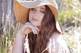 Young woman, brunette long hair, wears a floppy hat, surrounded by long grass, summer, countryside