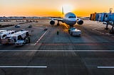 An aircraft sitting idle on the tarmac, in front of a deep, orange sunset.