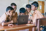 5 orang anak SD yang sedang melihat layar laptop macbook di kelas. foto ini mengilustrasikan pentingnya learn, unlearn, dan relearn dalam proses belajar