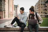 Two college students sitting on a concrete bench.