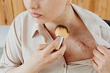 Woman applying makeup to scar on chest