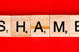 Scrabble tiles spell out the word “Shame” on a red background.