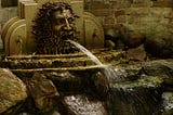 A fountain with a demonheaded figure shooting a stream of water out of its mouth onto the rocks below