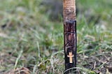 Photo of a wooden stake with carvings on it stuck into the ground against a background of grass.