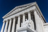 The United States Supreme Court building is photographed from below, showcasing its Greek architecture.