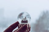 A hand holding a glass snow globe with a house inside.