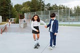 Girl Holding the Hand of a Boy While Riding a Skateboard