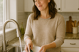 A woman hums to herself while washing dishes.
