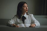 A lady in white with a book on her desk but pondering her next move