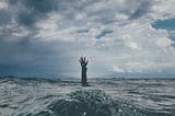 A hand is seen asking for a help on a wavy ocean.