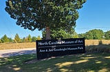 A sign that says ‘North Carolina Musuem of Art’ in front of a tree