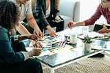 Four colleagues working together, gathered around a coffee table covered in paper and notes.