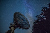 Large radio telescope set against a night sky full of stars, with the Milky Way galaxy visible in the background