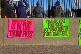 Protesters in St. Louis stand with their backs to camera behind two colorful signs that read: “Epstein Is In The Trump Files” and “Thank You For Your Attention To This Matter.” (Photo by author.)