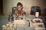 Boy sitting at at table with a birthday cake and party decorations.