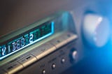Image shows part of the blue display of a silver-colored stereo tuner.