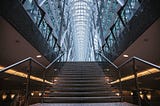 Stone stairs with railing on either side. Vaulted glass ceiling above stairs.