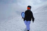 Snowboarder on top of mountain walking with snowboard in hand.