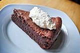 A slice of chocolate tart topped with a scoop of whipped cream