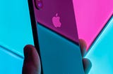 Photo of someone holding an iPhone against a neon background, taken by Daniel Korpai on Unsplash.
