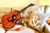 Picture of guitar and a pillow with an ampersand sitting on a couch